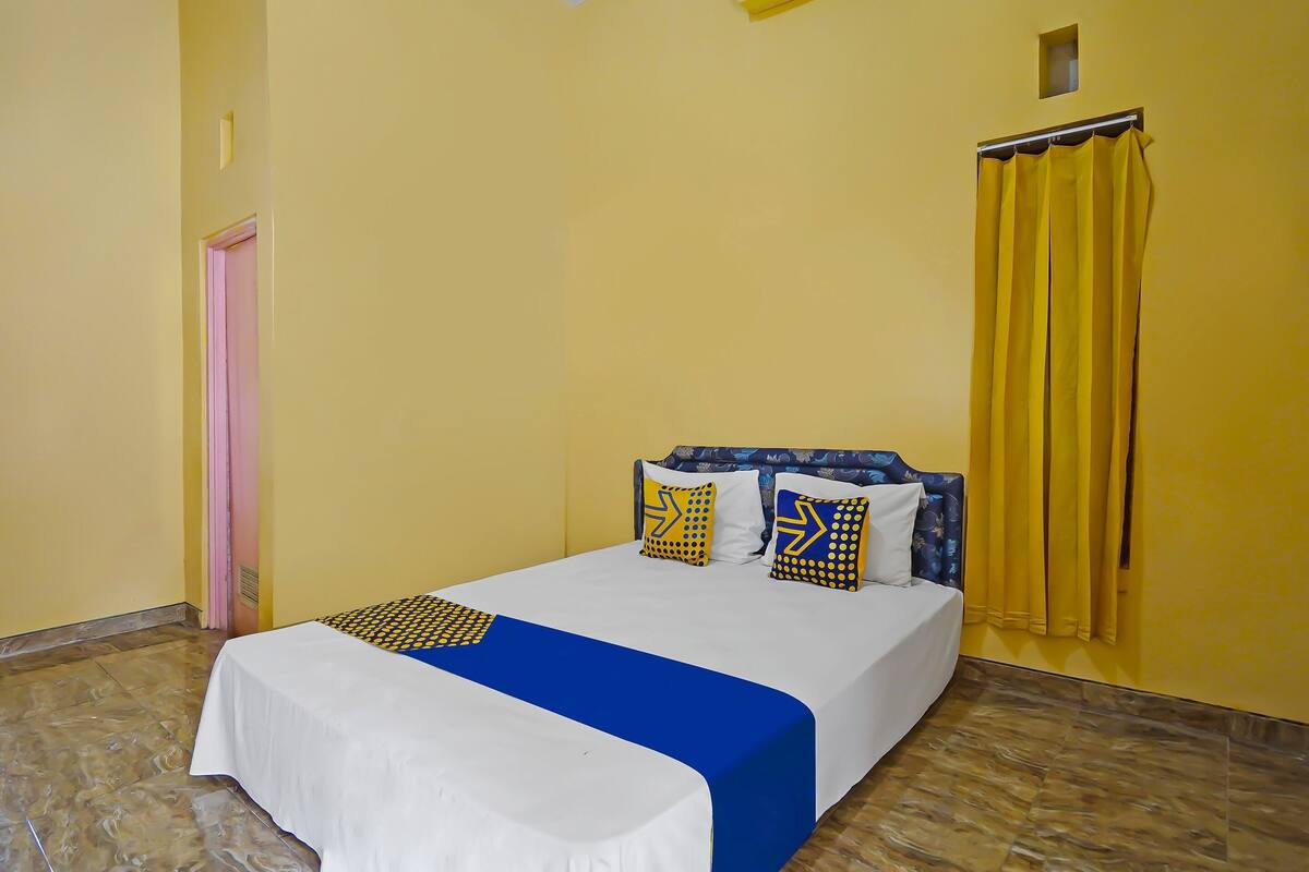 A room with a bed, yellow walls, a pink door, and a window with yellow curtains.