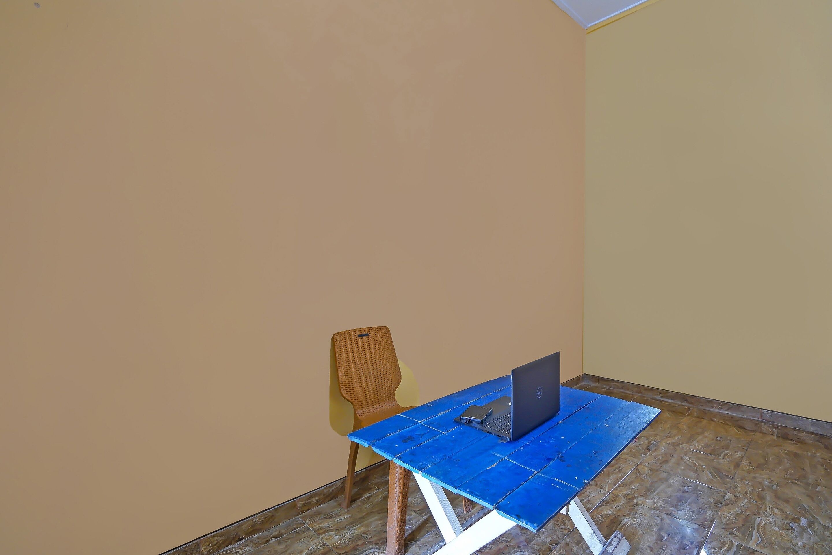 A small room with a blue table, a laptop, and a wicker chair.
