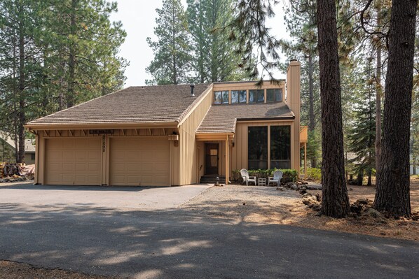 A two-story house with a garage, surrounded by tall pine trees.