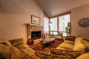 A living room with a fireplace, sofas, a coffee table, and a large window with blinds.