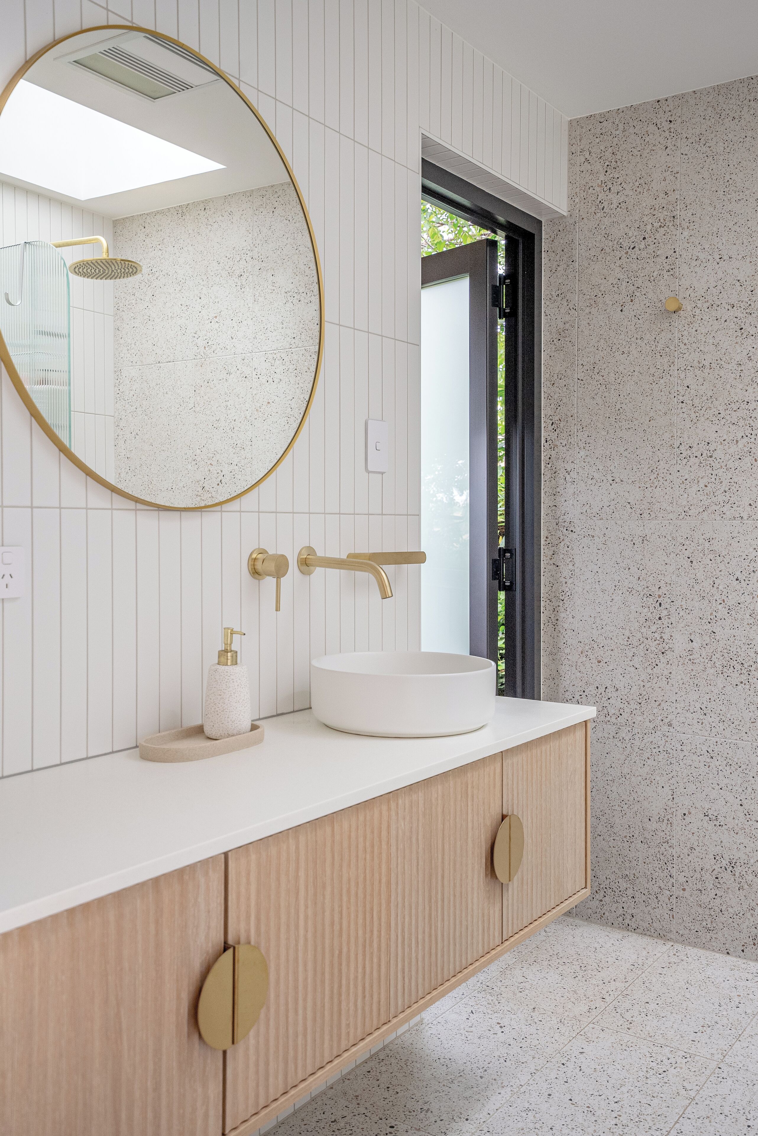 Une salle de bain moderne avec un miroir rond, un lavabo blanc et des meubles en bois.