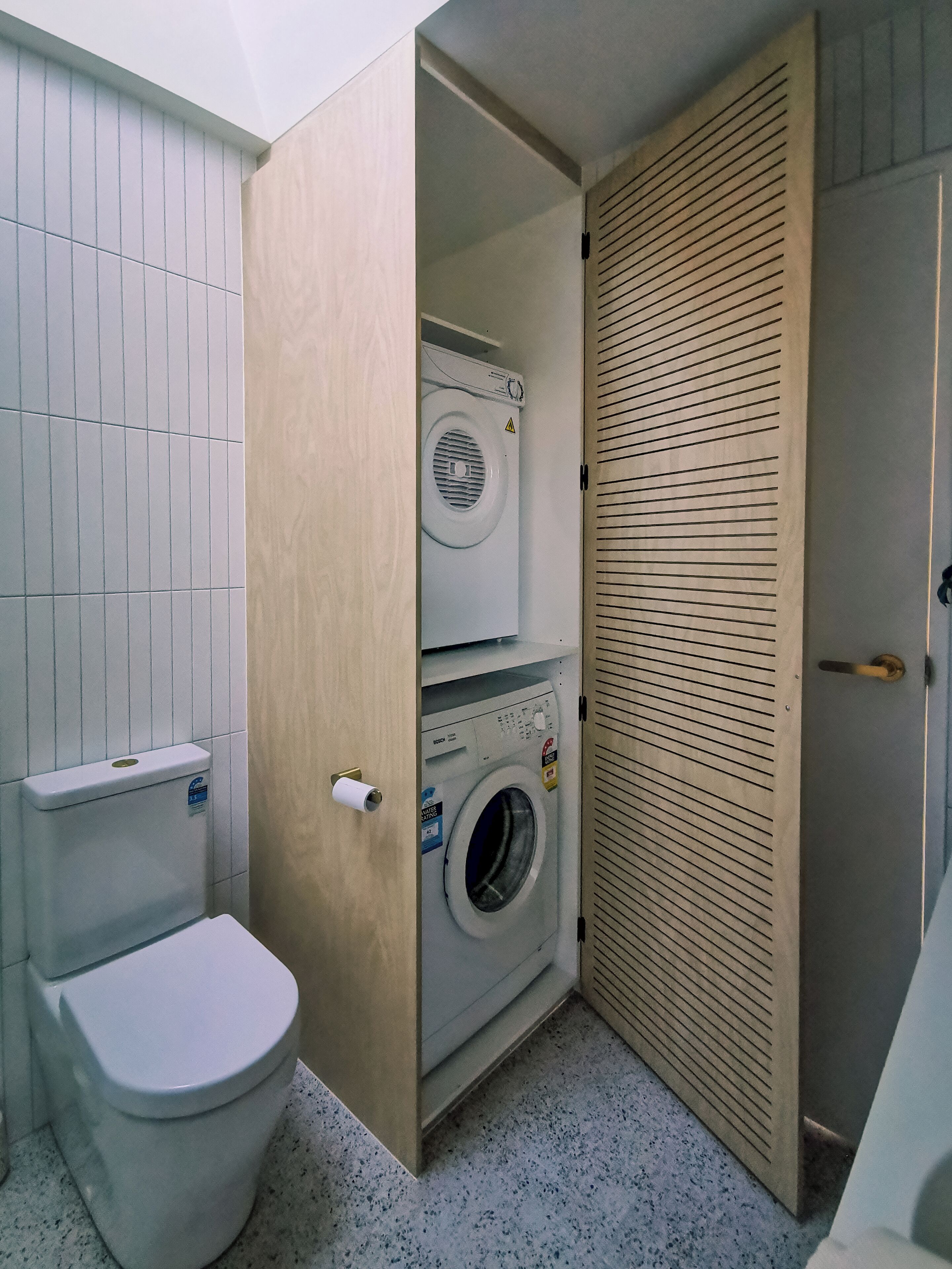A compact bathroom with a toilet, a washing machine, and a wooden door.