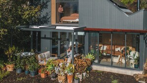 A modern house with a large glass facade, a balcony, and a garden area with potted plants. - Wren House Victor Harbor (Victor Harbor)