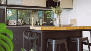 A modern kitchen with wooden ceiling, a large island with stools, and a view of greenery outside. - Wren House Victor Harbor (Victor Harbor)