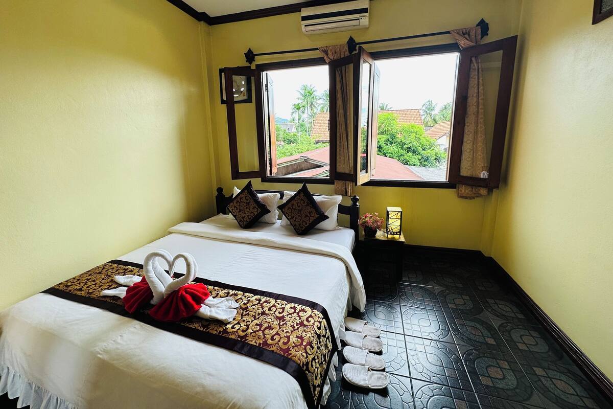 A hotel room with a bed, two windows, a nightstand, and a decorative wall piece.