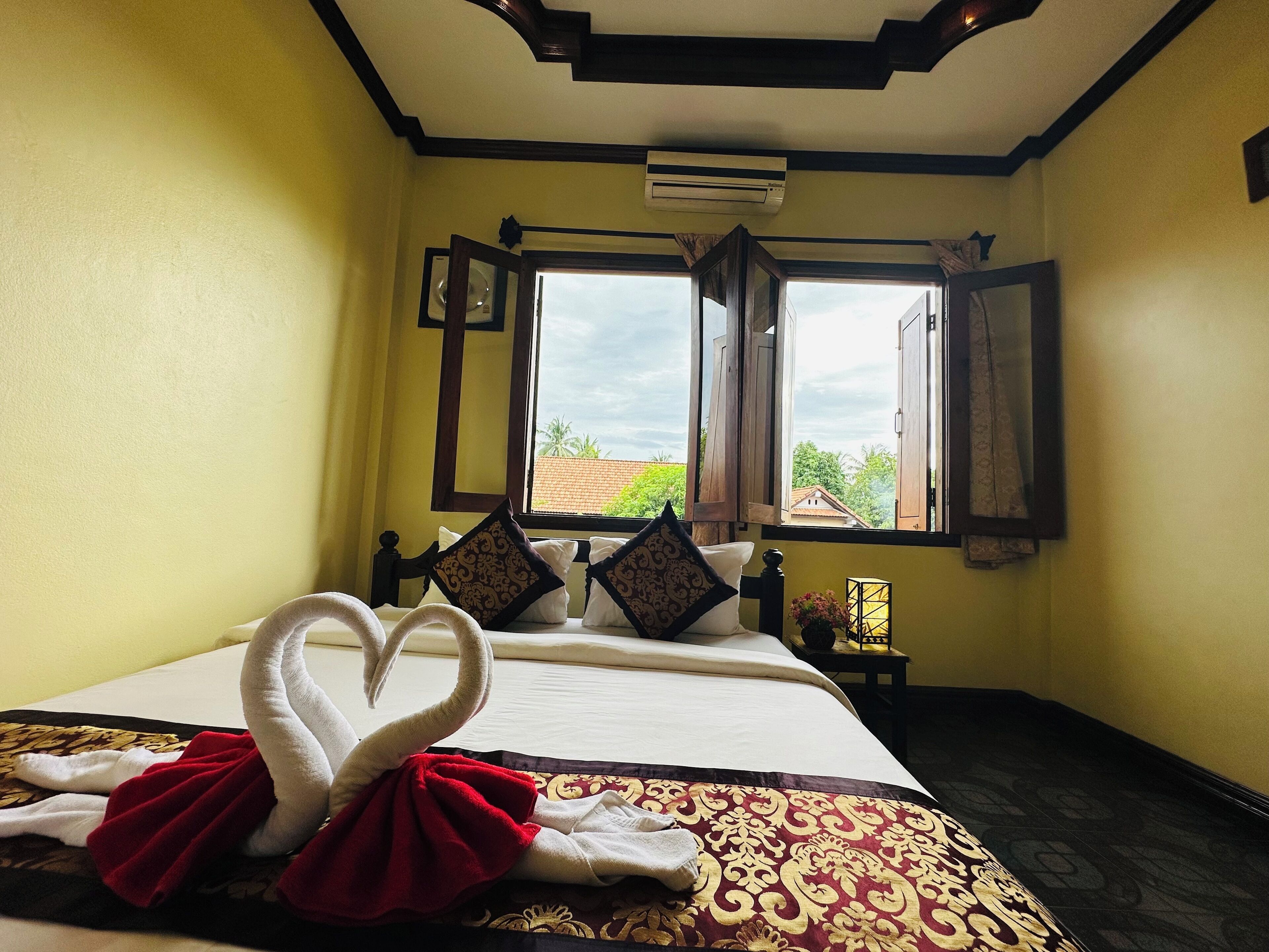 Une chambre d’hôtel avec un lit, une fenêtre dont les volets sont ouverts, et une vue sur la verdure.