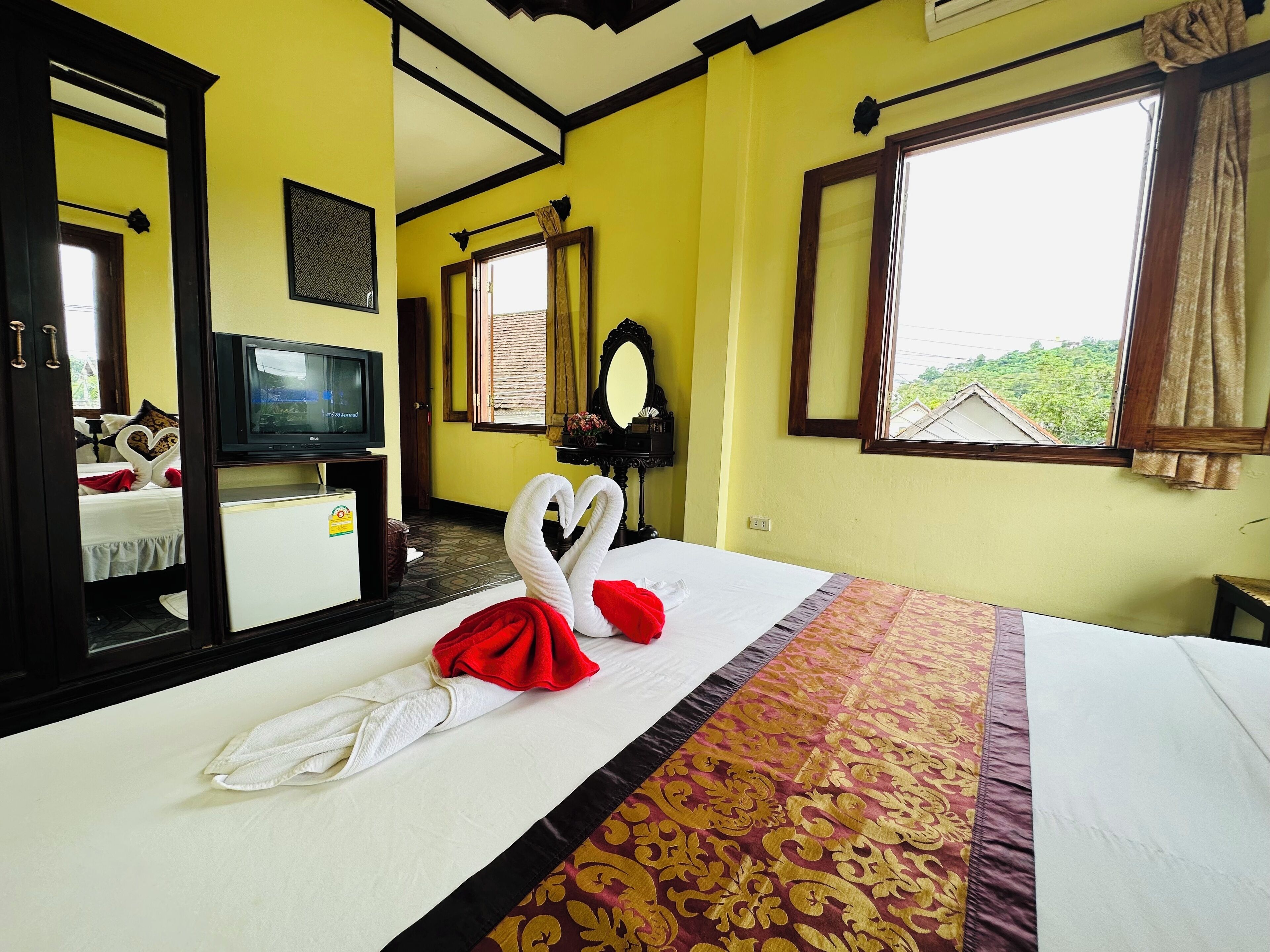 Habitación de hotel con cama, televisión, espejo y ventana con vista a vegetación.