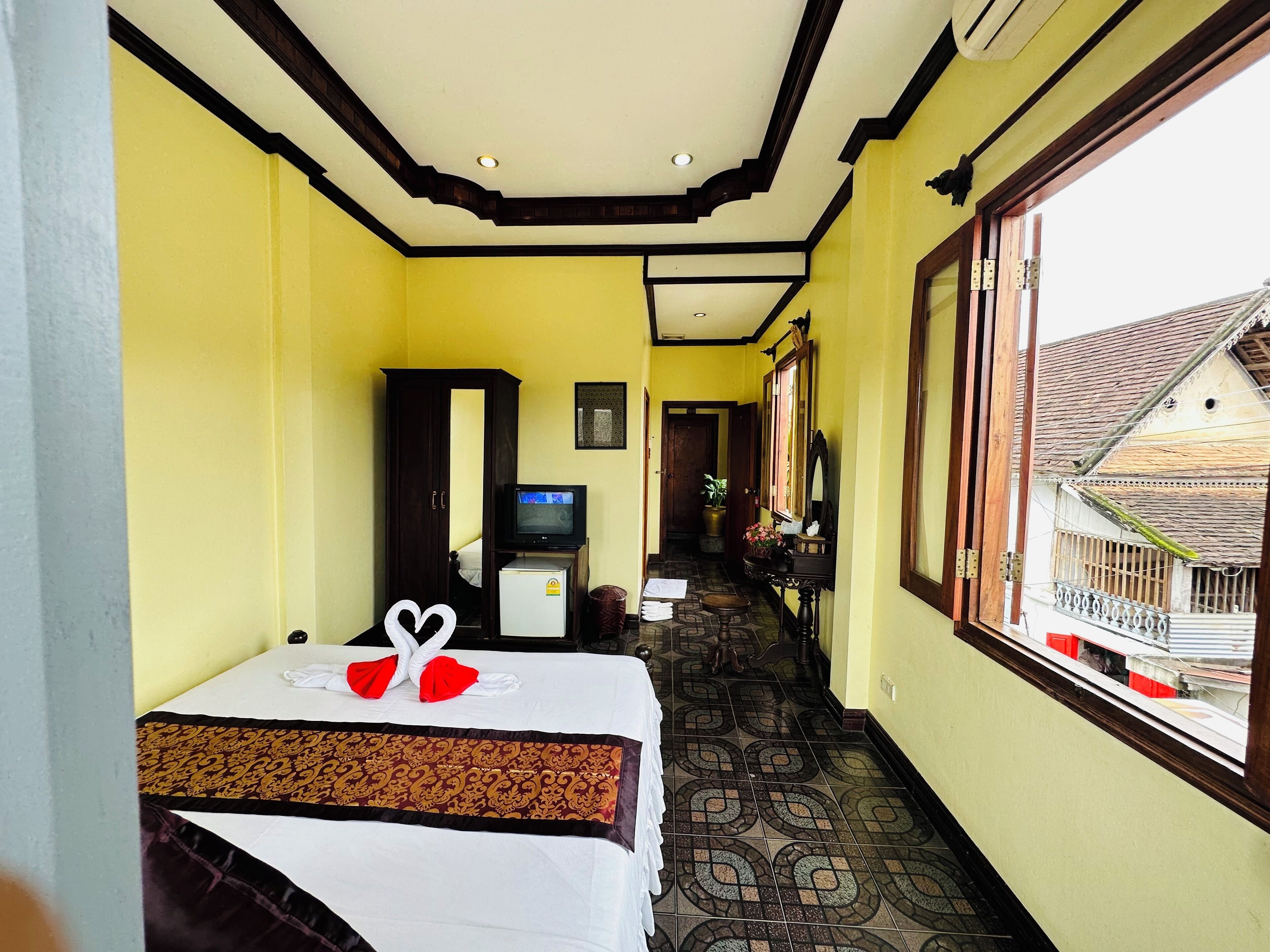 A hotel room with a bed, a television, a small refrigerator, and a window with a view of buildings outside.