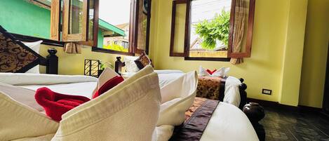 A hotel room with two beds, a green wall, and a window with a view of greenery outside.