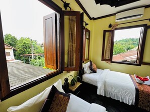 Een kamer met twee bedden, een raam met open luik en uitzicht op groen.