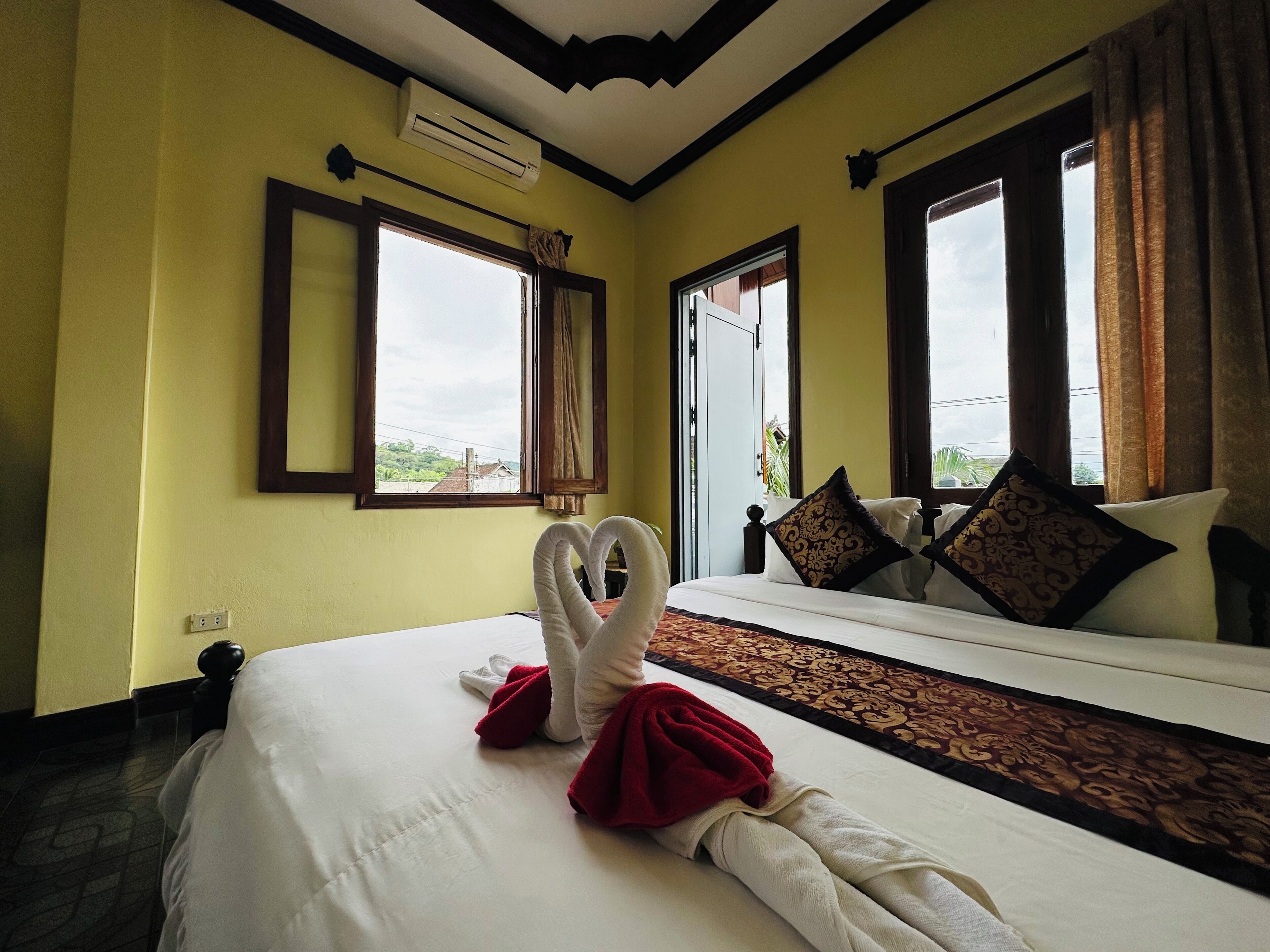A hotel room with a bed, two windows, an air conditioner, and a view of the outside.