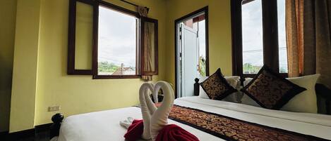 A hotel room with a bed, two windows, an air conditioner, and a view of the outside.