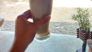 A hand holding a glass with a straw, a beach view, and a thatched roof structure.