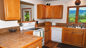 A kitchen with wooden cabinets, a stove, a dishwasher, and a window with a view of greenery. - Mountain Lodge • New Hot Tub • Great Mountain Views • Firepit • Pet Friendly (Marble)