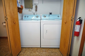A laundry room with two stacked washers and dryers, a fire extinguisher on the wall, and a toilet paper roll on the left.