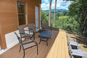 A wooden deck with outdoor furniture, a view of a mountainous landscape, and a building with a door and windows.