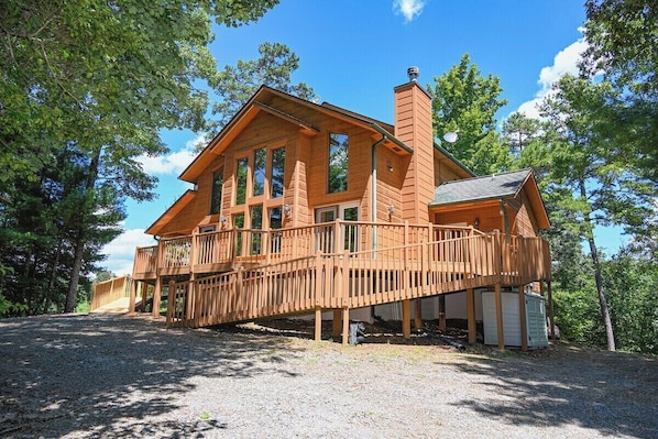 A two-story wooden cabin with a balcony, surrounded by trees.