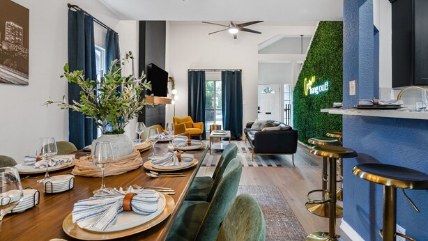 A modern dining area with a long table set for a meal, a sofa, and a bar area with stools.