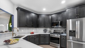 A modern kitchen with dark cabinetry, stainless steel appliances, and a marble countertop.