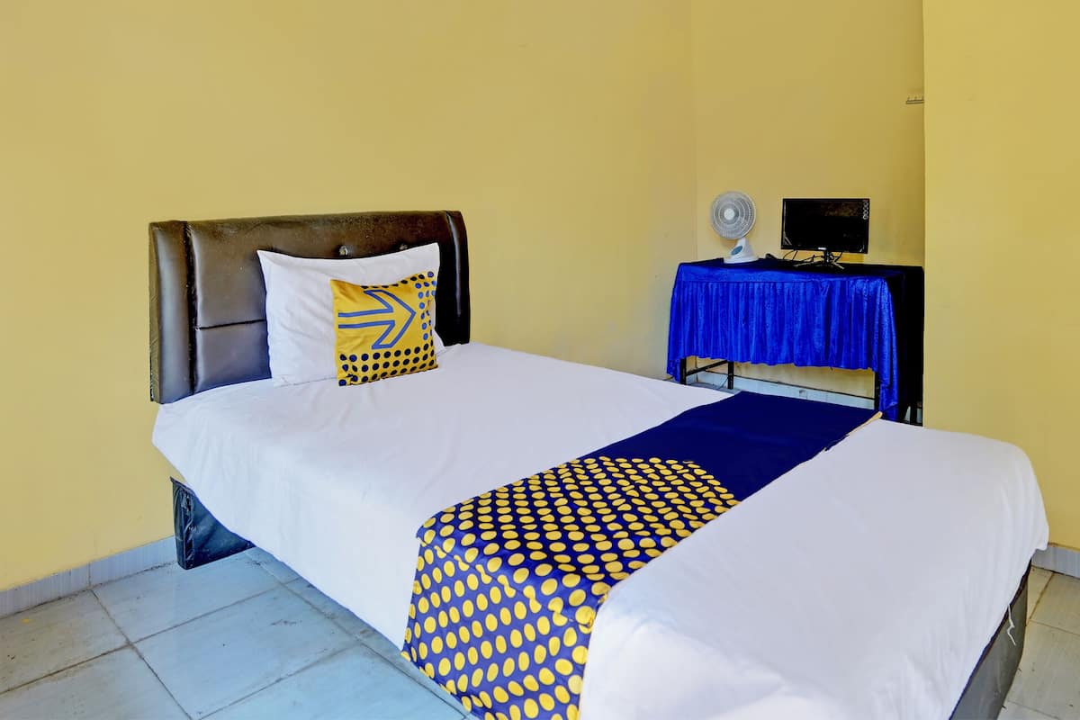 Ein ordentlich gemachtes Bett mit weißblauer Bettdecke, einem gemusterten Kopfkissen und einem blauen Nachttisch mit Ventilator und schwarzem Gerät.