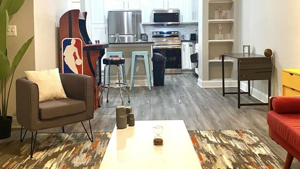 A modern living room with a white coffee table, a sofa, and a red armchair. There is a kitchen in the background with white cabinets and stainless steel appliances. - SUAVE&SPACIOUS SUITE NEAR EVERYTHING (Atlanta)