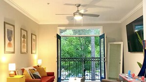 A room with a ceiling fan, a view through a glass door to a balcony, a sofa, a table with a lamp, and framed pictures on the wall. - SUAVE&SPACIOUS SUITE NEAR EVERYTHING (Atlanta)