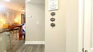 A hallway with a beige wall and a door on the right. There are three signs on the wall: 'Live Laugh Love', 'Start each day with a Grateful Heart', and an NBA logo. - SUAVE&SPACIOUS SUITE NEAR EVERYTHING (Atlanta)