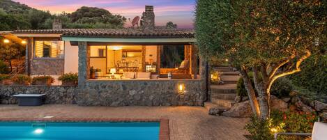 A modern villa with a stone exterior, a swimming pool, and a patio area with outdoor furniture.