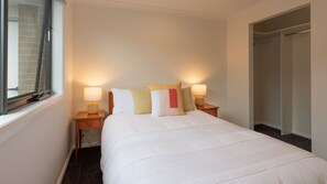 Ein ordentlich bezogenes Bett mit weißer Bettwäsche und vielen Kissen in einem Hotelzimmer.