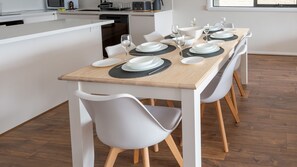Enjoy meals in this stylish kitchen with a stainless steel range hood, white cabinetry, and a dining table set for a meal.
