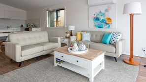 Relax in a spacious living room with a comfortable sofa, coffee table, and floor lamp, offering a view of the outside.
