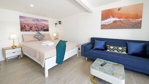 A bedroom with a bed, bedside tables, a blue sofa, and two paintings on the walls. - Mentone Compact Backyard Cabin Beachside (Parkdale)