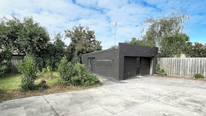 A modern house with a dark brick exterior, a garage door, and a concrete driveway. - Mentone Compact Backyard Cabin Beachside (Parkdale)