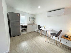A compact kitchen with a refrigerator, microwave, sink, and a small dining area with two chairs and a table. - Mentone Compact Backyard Cabin Beachside (Parkdale)