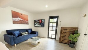 A living room with a blue sofa, a coffee table, a TV mounted on the wall, a wooden cabinet, and a door with a window. - Mentone Compact Backyard Cabin Beachside (Parkdale)