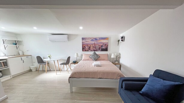 A modern bedroom with a bed, a blue sofa, a desk with chairs, a small table, and a painting on the wall. - Mentone Compact Backyard Cabin Beachside (Parkdale)