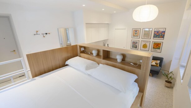 A modern hotel room with a large bed, wooden headboard, bedside tables, a wardrobe, a mirror, and artwork on the wall. - Torlonia Studio in Rome (Rome)