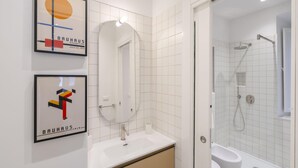 A modern bathroom with a white sink, mirror, and toilet. There are framed artworks on the wall and a shower area visible through an open door. - Torlonia Studio in Rome (Rome)