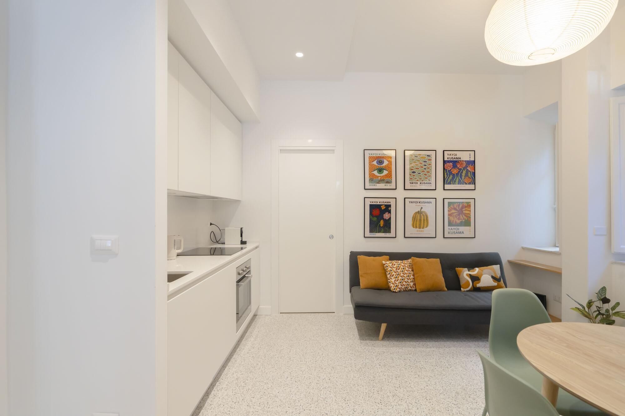 A compact living space with a kitchenette, a sofa with patterned cushions, and a dining area with a table and chairs.