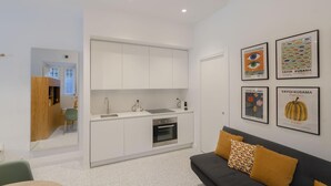 A modern kitchen with white cabinets, a built-in oven, and a sink. There is a dining area with a table and chairs, and a sofa with cushions. - Torlonia Studio in Rome (Rome)