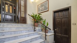 A marble staircase leading to a dark wooden door, with a potted plant on the landing and a framed picture above the door. - Torlonia Studio in Rome (Rome)