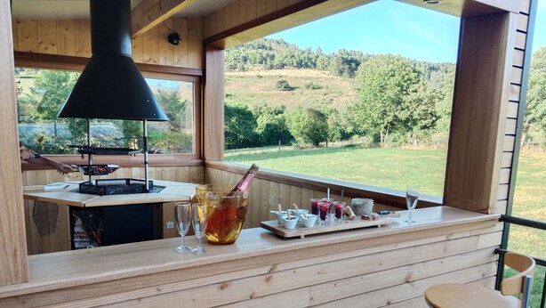 Eine Holztresore mit Blick auf eine grüne Landschaft, eine Champagnerflasche, Gläser und ein kleiner Grill.