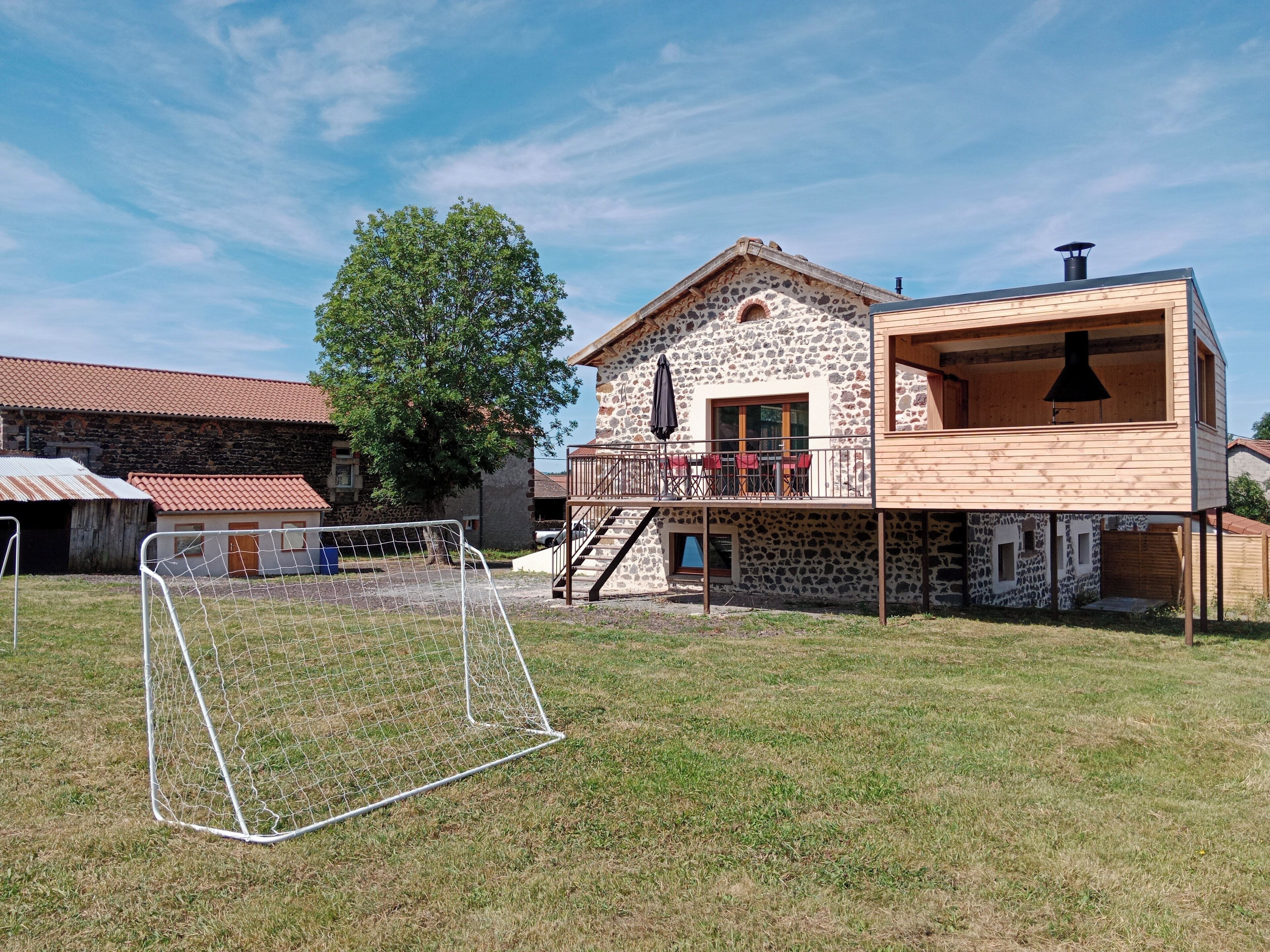 Un bâtiment en pierre doté d’une terrasse en bois et d’un balcon, entouré d’une pelouse et d’un but de football.