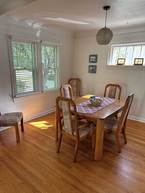 A dining area with a wooden table and chairs, a woven chair back, a hanging light fixture, and a window with blinds. - Quaint sunny cottage that rests in the historical neighborhood of Billings (Billings)