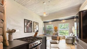 A modern kitchen with a gas stove, wooden cabinets, and a dining area with a sofa and table. - ★ HostWise Stays ★ 2 Apartments in 1 - Great Privacy, Beautiful Space! (Pittsburgh)