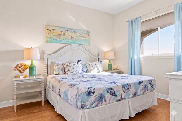 Un dormitorio con una cama, dos mesitas de noche, un velador, una ventana con cortinas y un cuadro en la pared.