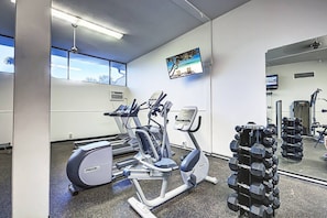 A gym with cardio equipment, a mirror, and a TV on the wall. - Fully Renovated Condo on Bay | Resort Amenities (Siesta Key)