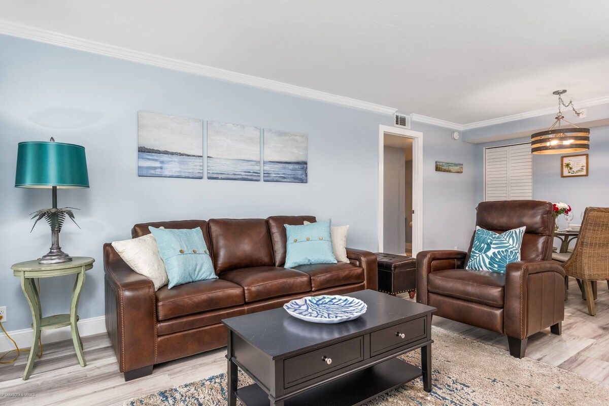A living room with a brown leather sofa, a matching armchair, a coffee table, and a side table with a lamp.