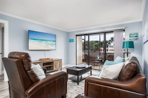 A living room with leather sofas, a flat-screen TV, a coffee table, and a view of the beach through a sliding glass door. - Fully Renovated Condo on Bay | Resort Amenities (Siesta Key)