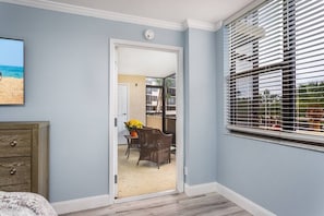 A room with a door leading to a balcony, a window with blinds, and a wall-mounted clock.